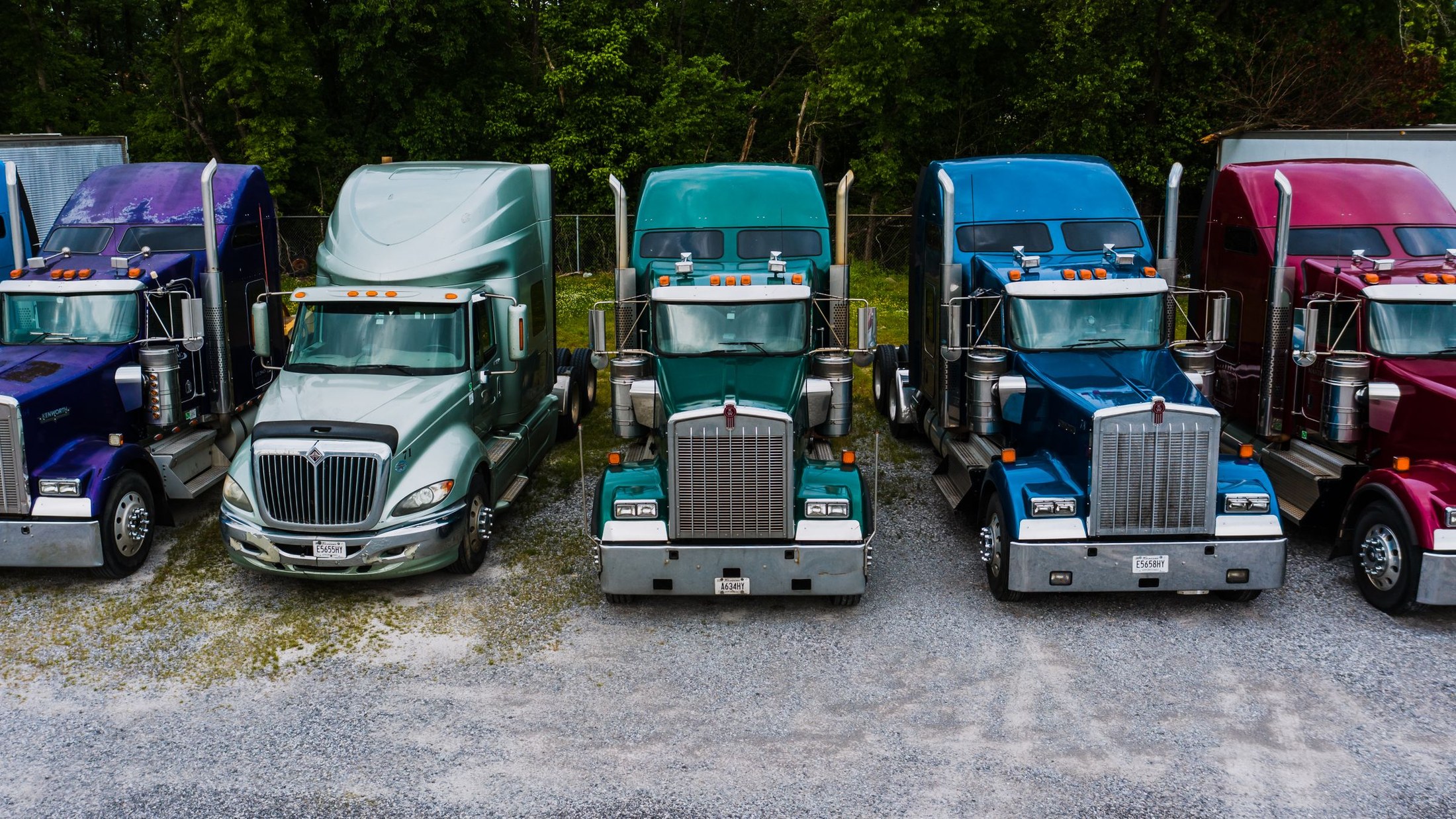 Front views of colorful American semi trucks parked in an outdoor yard.