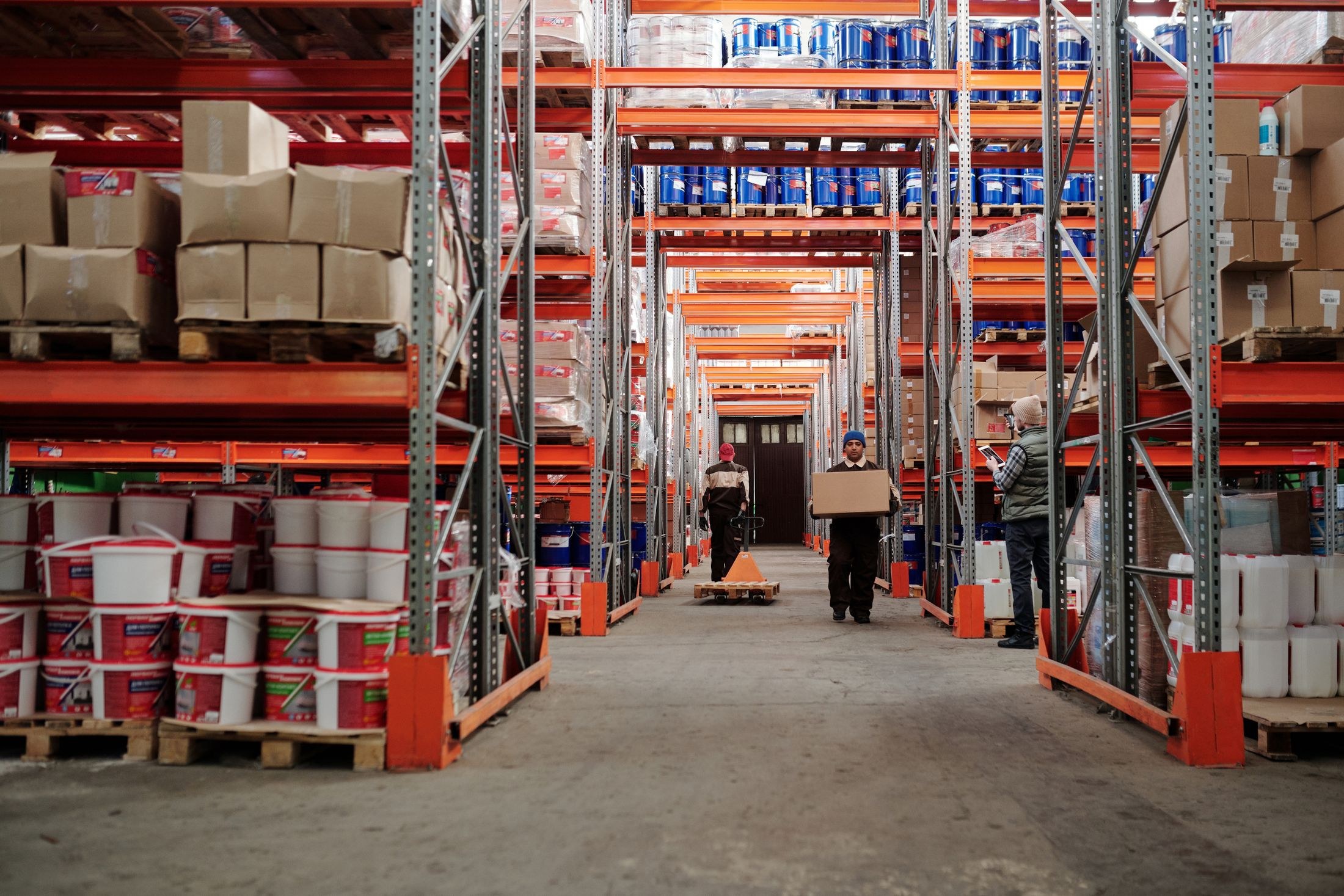 Warehouse employees moving cartons and checking stock among loaded storage racks.